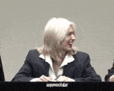 a man with long blonde hair is sitting at a table with a sign that says aspenrockstar on it