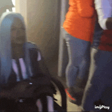 a woman with long blue hair is sitting in a chair next to a man in an orange shirt .