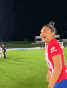 a woman in a red hyundai shirt is laughing on a soccer field at night