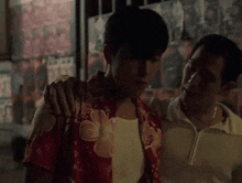 a man in a red shirt holds another man 's arm over his chest