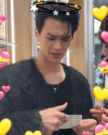 a man wearing a black sweater is holding a piece of paper with hearts around him