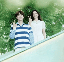 a man in a blue and white striped shirt stands next to a woman in a white dress giving a peace sign