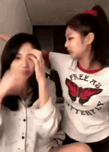two young women are sitting next to each other in a room . one of the girls is wearing a butterfly shirt .
