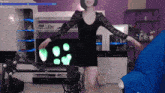 a woman in a black dress is dancing in front of a microphone in a living room