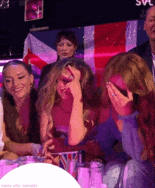 a group of women are sitting at a table and one of them is covering her eyes with her hand