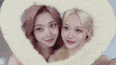 two women are taking a selfie with a heart shaped frame .