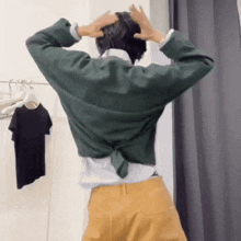 a woman in a green shirt and yellow pants is standing in a dressing room with her hands on her head