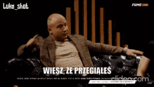 a man in a suit is sitting on a couch with a foreign language caption