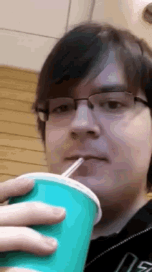 a man wearing glasses is drinking from a green cup with a straw