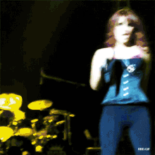 a woman in a corset is standing on a stage with a drum set in the background
