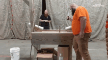 a man in an orange shirt holds a knife in front of a screen that says " awesome "