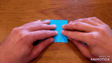 a person is folding a piece of blue paper on a wooden table