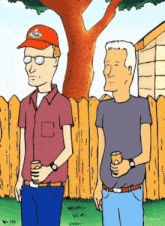 two men standing next to each other in front of a fence and a tree