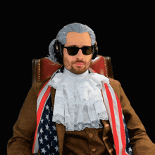 a man in a wig and sunglasses is sitting in a chair with an american flag around his neck