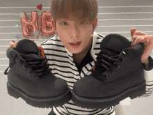 a young man holds up a pair of black boots in front of a pink hb balloon