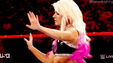 a woman in a pink and black outfit is standing in a ring with her hands outstretched .