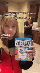 a woman is holding a box of fruit snacks and a man is standing behind her