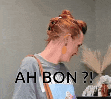 a woman with red hair is wearing a gray shirt and a brown bag and making a funny face .