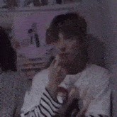 a young man wearing a striped shirt and a necklace is sitting in a room .