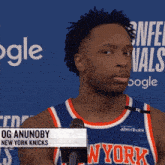 a man in a new york knicks jersey stands in front of a blue background