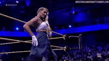a woman is standing in a wrestling ring with her arms outstretched in front of a crowd .