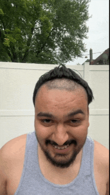 a man with a shaved head and a beard wearing a grey tank top