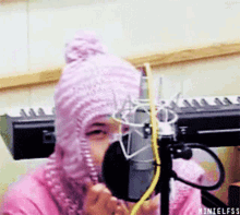 a person wearing a pink knitted hat is singing into a microphone in front of a keyboard