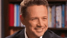 a man in a suit and white shirt is smiling in front of a book shelf .