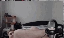 a man laying on a bed with a microphone in front of him and two cats