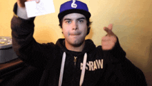 a man wearing a hoodie that says raw holds up a piece of paper