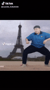 a man in a blue shirt is dancing in front of the eiffel tower on a tiktok video