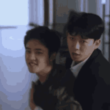 two young men are standing next to each other in a hallway and looking at the camera .