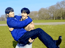 a man is carrying another man in his arms in a park