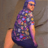 a man wearing a colorful shirt and sunglasses is squatting