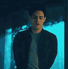 a man in a black jacket is standing in front of a blue curtain .