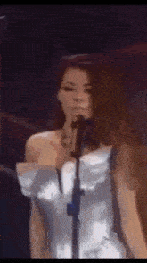 a woman in a white dress is singing into a microphone in a dark room .