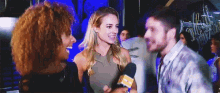a man and two women are talking to each other in a club while a woman holds a microphone .