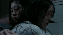 a woman with a bandage on her arm is hugging another woman in the dark