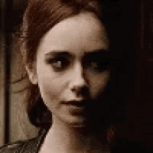 a close up of a woman 's face with red hair and a dark background .