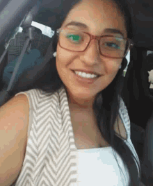 a woman wearing glasses and a chevron vest is smiling in a car