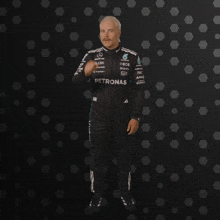 a man wearing a petronas racing suit stands in front of a black background