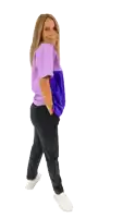 a woman wearing a purple top and black pants is standing with her hands in her pockets