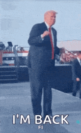 a man in a suit and tie is standing on a stage holding a microphone and saying i 'm back .