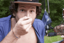 a man wearing a hat and a blue shirt is covering his mouth with his hand