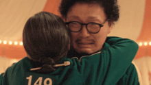 a man wearing glasses is hugging a woman wearing a green jacket with the number 140 on it