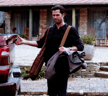 a man in a black shirt is carrying a brown bag and a jacket
