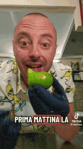 a man in a banana shirt is holding a green apple in his hand with the caption prima mattina la