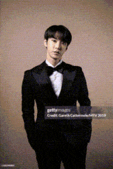 a young man in a tuxedo and bow tie is standing with his hands in his pockets