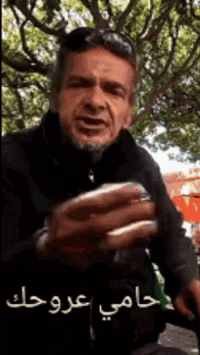 a man with a beard is holding a sandwich in his hand and talking in arabic .