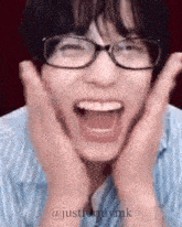 a young man wearing glasses is making a funny face with his hands on his face .